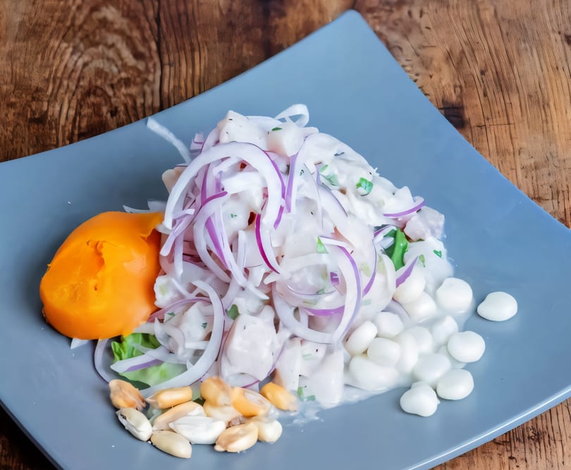 Peruvian ceviche with fish, red onion, sweet potato, corn, and toasted corn on a blue plate.